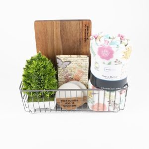 Personalized housewarming gift basket featuring a custom engraved cutting board, two engraved wooden coasters, a plush fleece blanket, and a scented candle.
