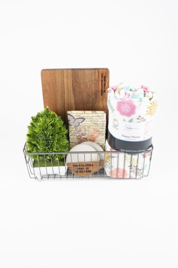 Personalized housewarming gift basket featuring a custom engraved cutting board, two engraved wooden coasters, a plush fleece blanket, and a scented candle.