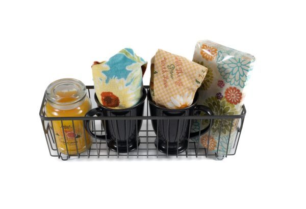 Housewarming gift basket with mugs candle and kitchen towels in a wire basket.