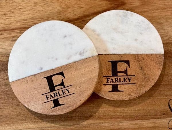 Pair of personalized marble and wood coasters with laser-engraved family name and monogram for a housewarming gift.
