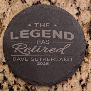 Pair of round black slate coasters laser engraved with The Legend Has Retired and personalized name and date.