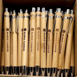 50 custom laser engraved wooden pens with company logo displayed on a professional desk.